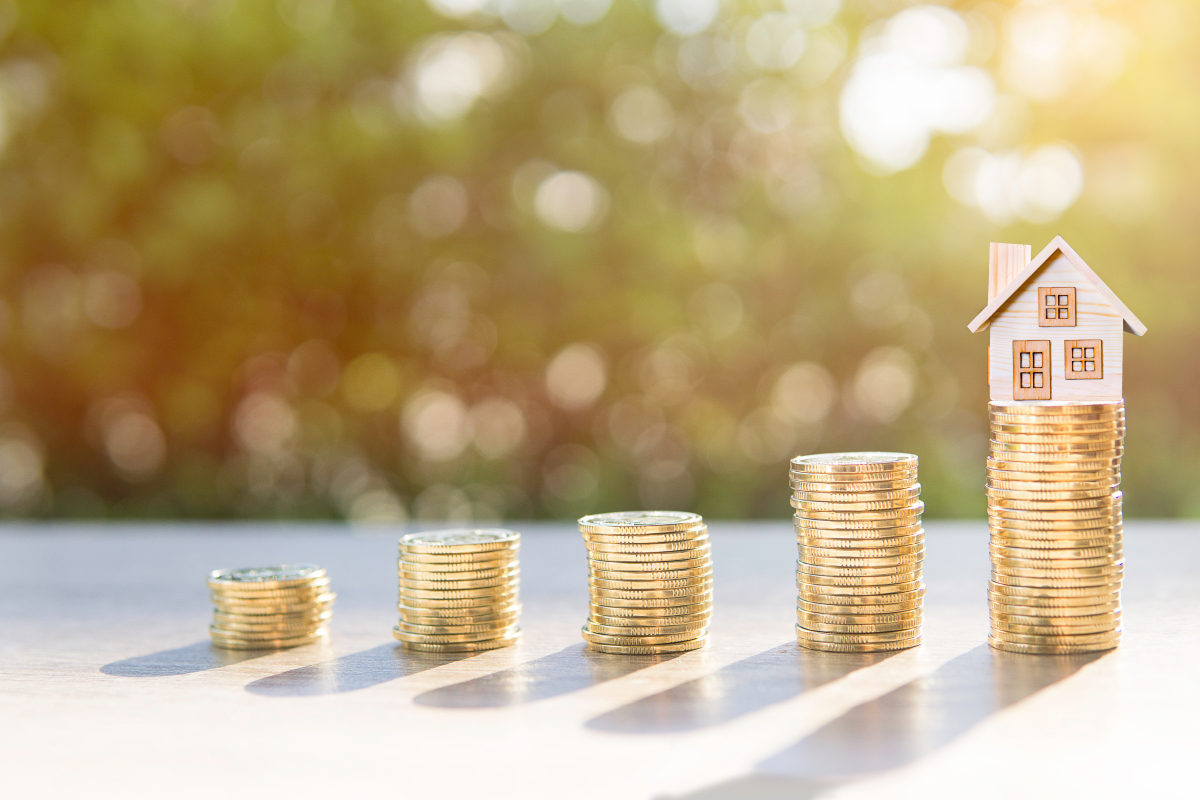 Assurance emprunteur – Les pièces sur le bois et la maison en arrière-plan clair présentent l'argent des économies ou des investissements