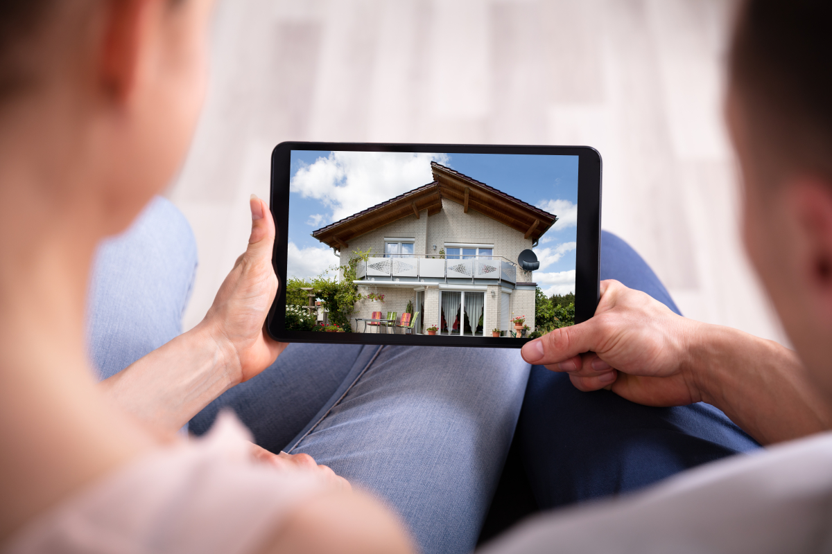 Avant la visite en présentiel la visite virtuelle peut être demandée Pass sanitaire et location – Couple en gros pan de dos regardant une maison sur tablette