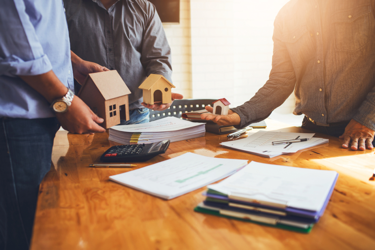 BEFA Définition — Des personnes tenant des maisons miniatures autour d’un bureau couvert de documents