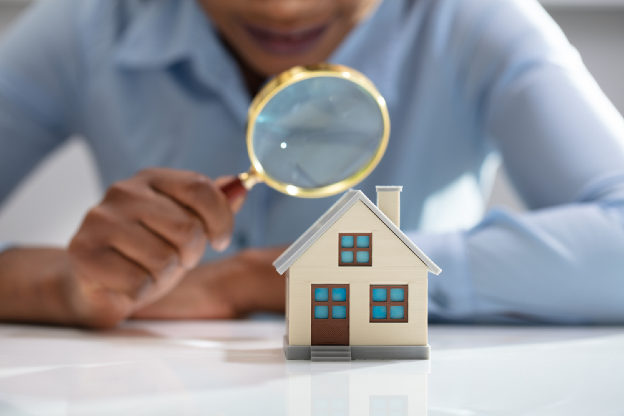 Un homme regarde une maison miniature à la loupe