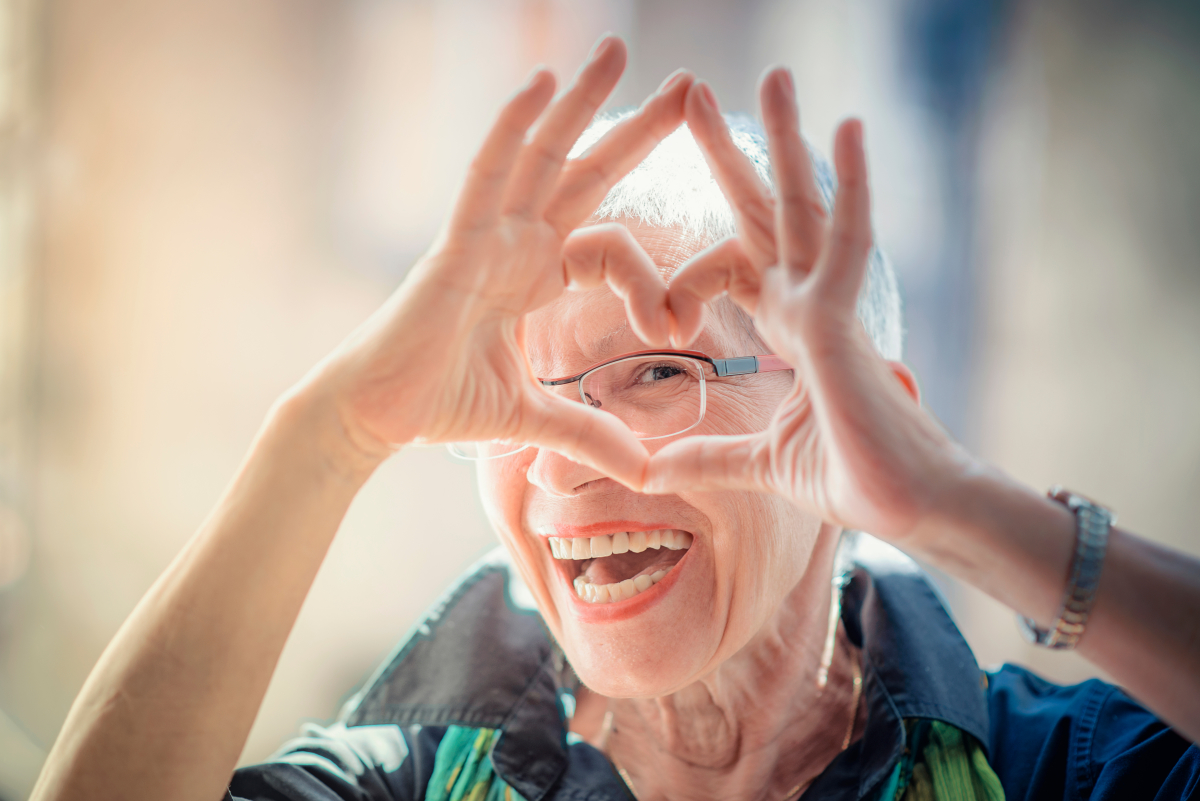 MaPrimeAdapt — Une femme âgée fait un cœur avec ses mains en regardant l’objectif de la caméra