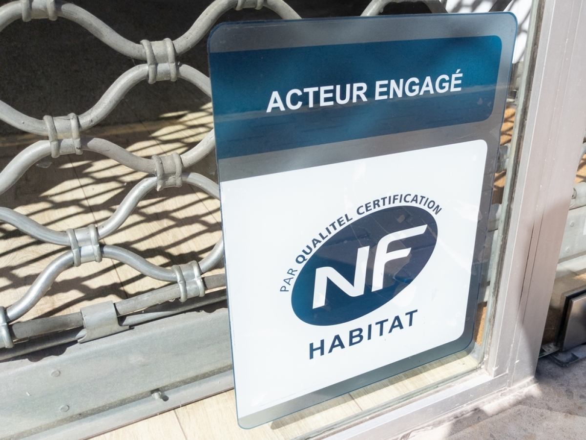 un panneau label NF habitat en bas d’un rideau métallique de commerce