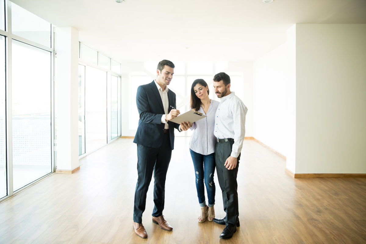 Vente achevée — un couple visite un appartement neuf vide accompagnés d’un courtier immobilier