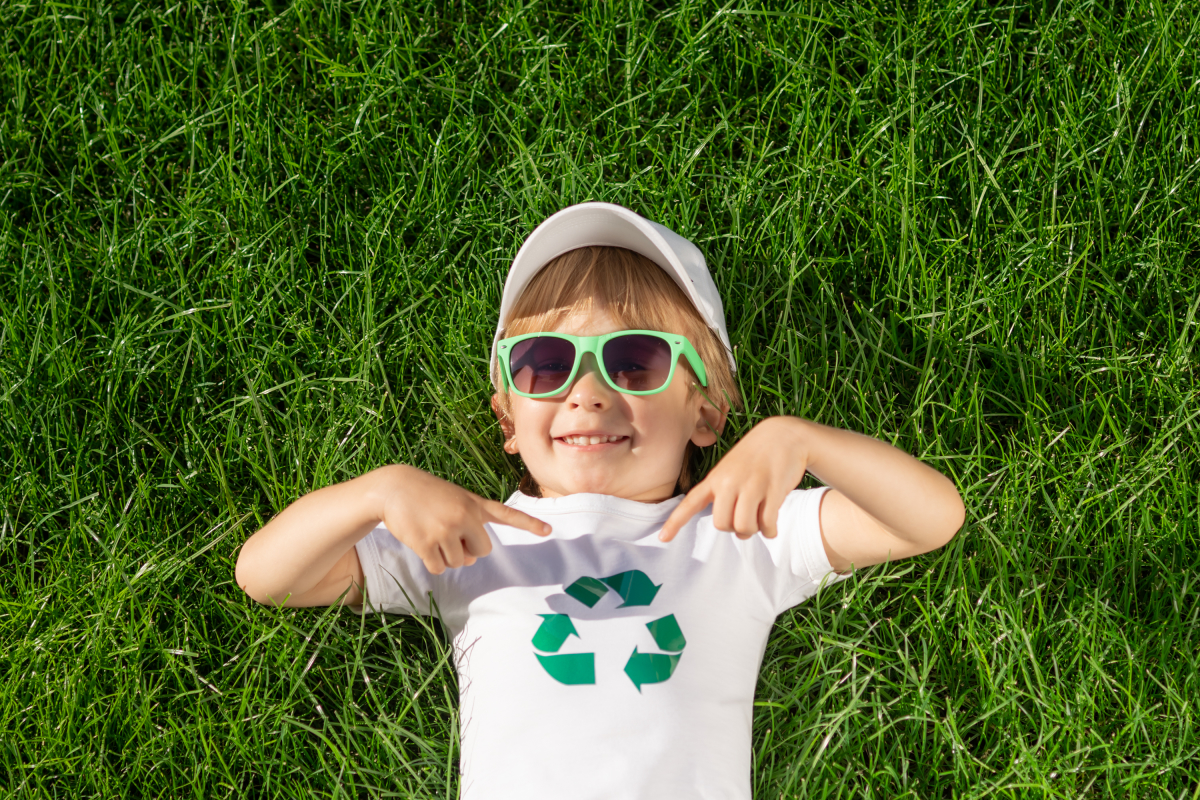 un enfant couché dans l’herbe avec des lunettes de soleil et un tee-shirt recyclé
