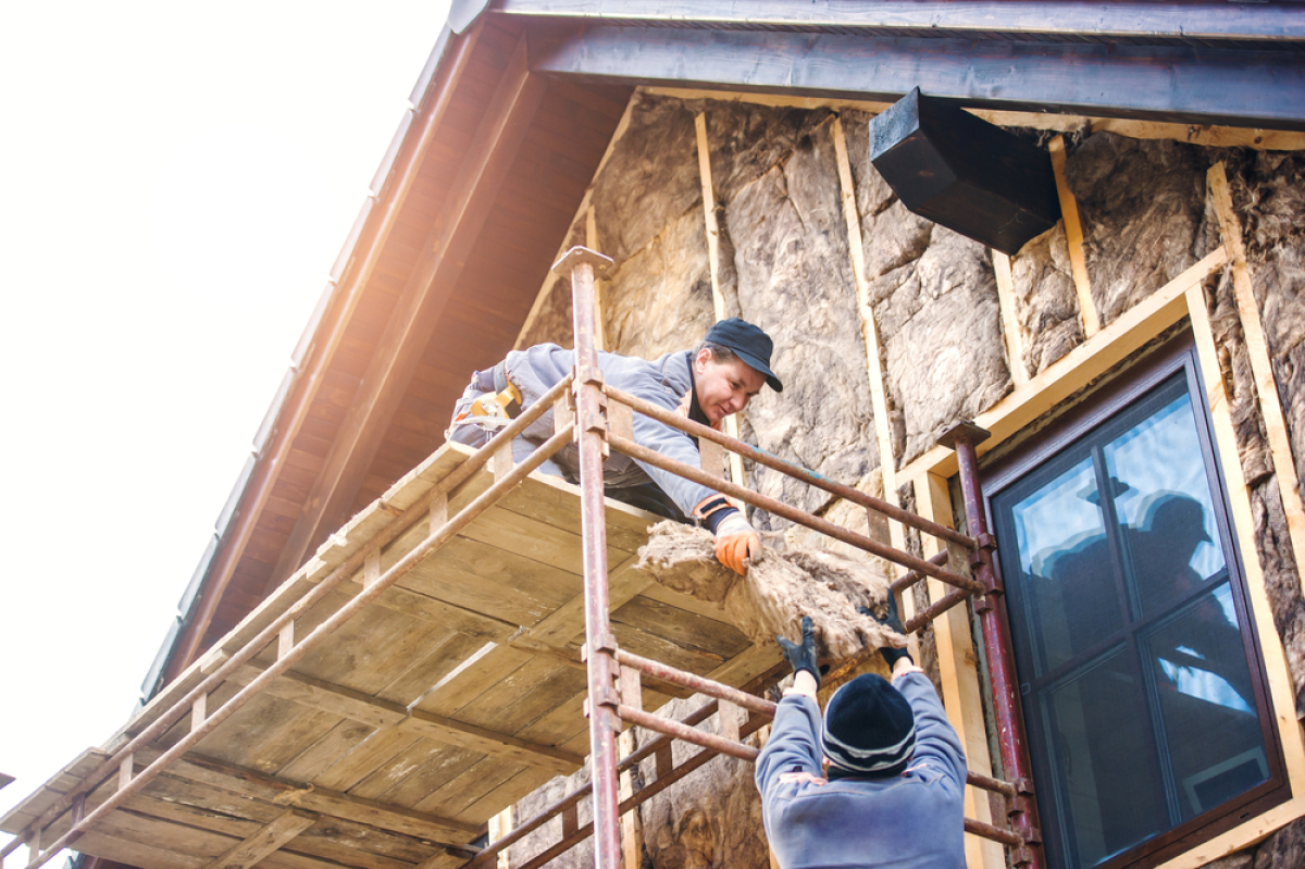 deux professionnels du bâtiment isolent la façade d’une maison avec de la paille