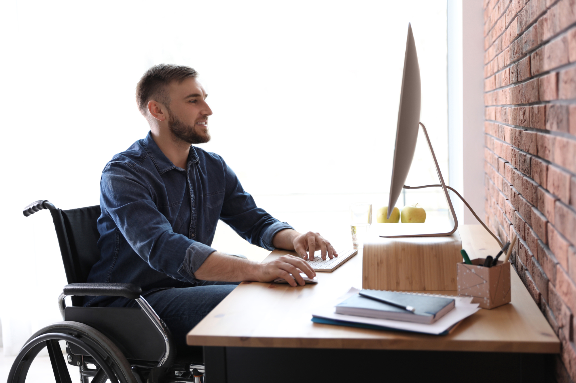 Une jeune homme en fauteuil roulant travaille sur son ordinateur
