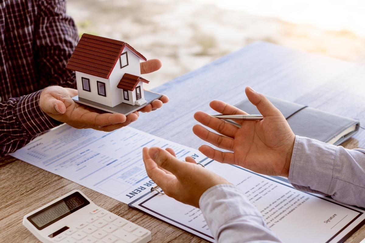 Comment donner congé à son locataire ? – Une personne tend une maison miniature à une autre au-dessus de contrats