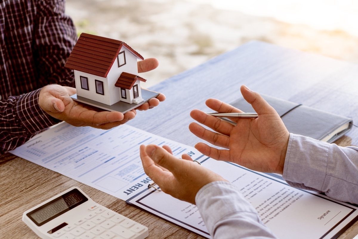 appartement invendu programme neuf – un homme signe un contrat immobilier pendant qu’un autre tend une maquette de maison