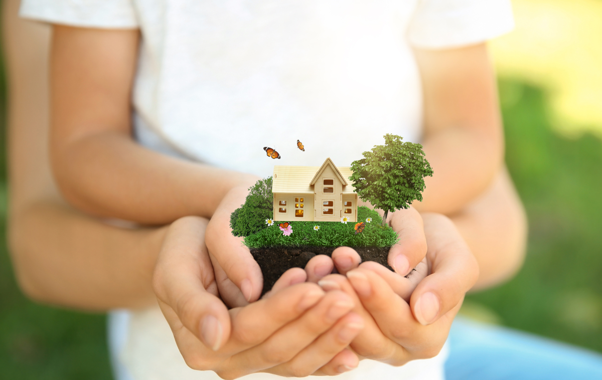 des mains d’enfants et des mains d’adulte entourant une petite maison de bois 