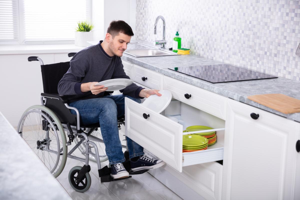 Réglementation PMR Logement — un homme en fauteuil roulant range sa vaisselle