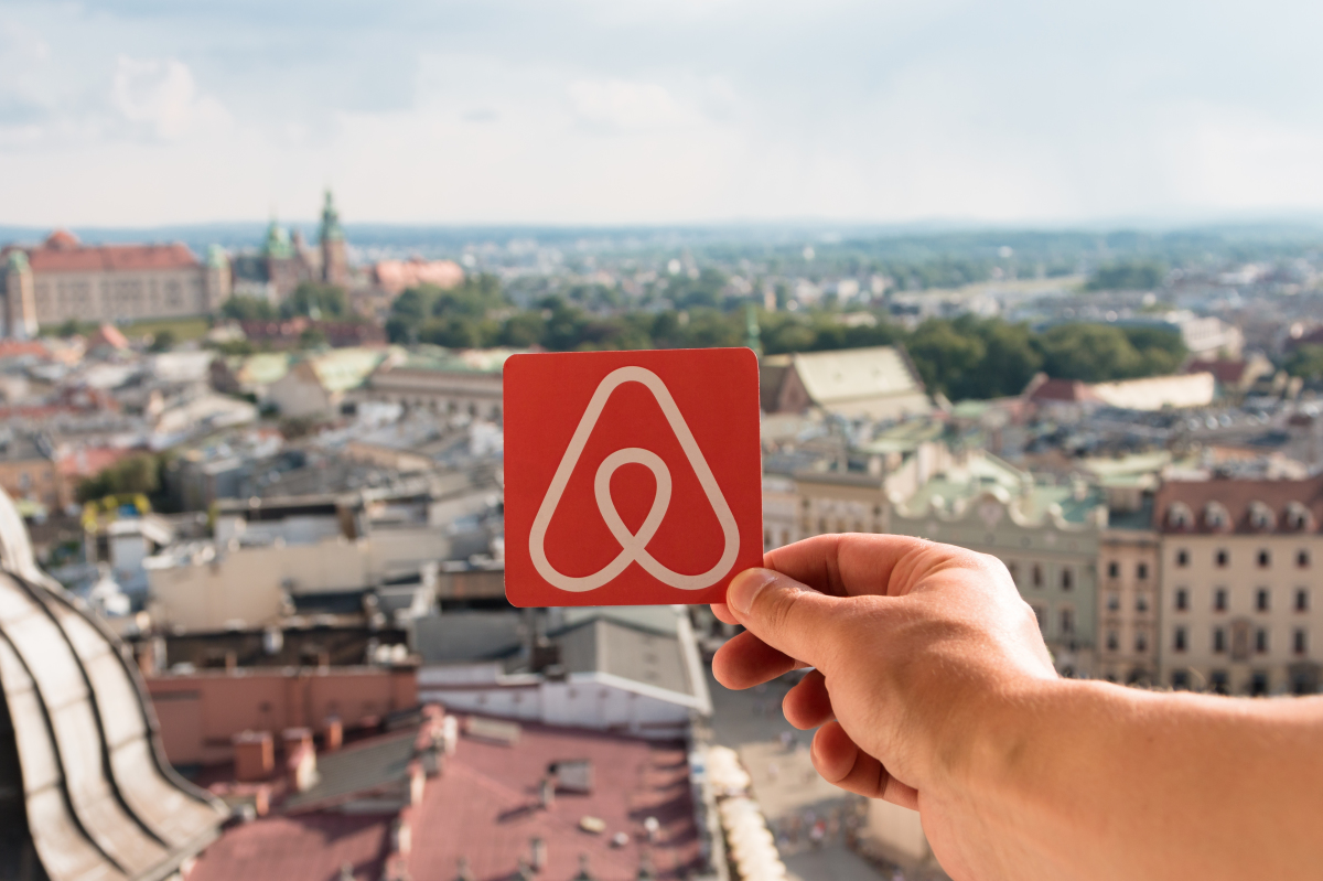 un logo air bnb tendu par une main sur fond de paysage urbain