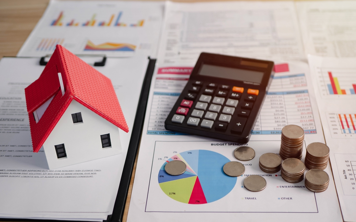 une calculette un tas de pièces et une maquette de maison au-dessus de documents papier