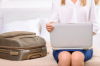 une femme avec un ordi portable et une valise assise sur un lit