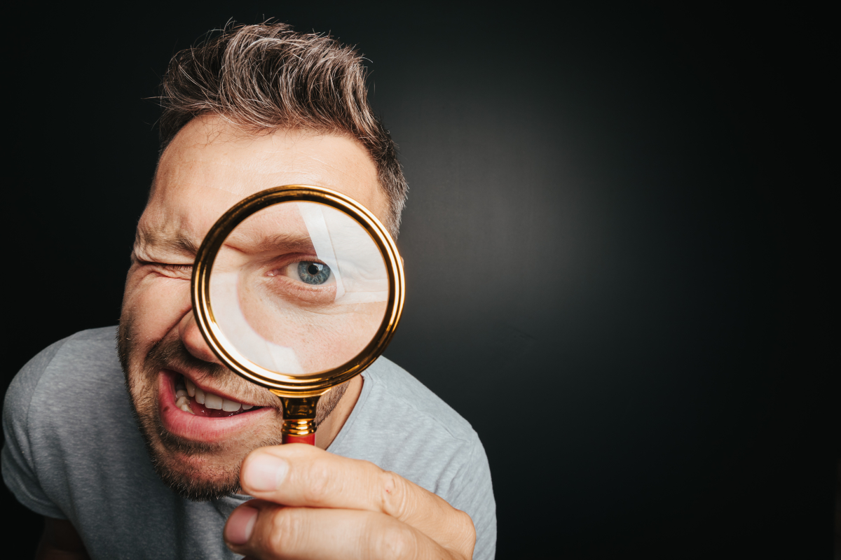 un homme grimaçant regardant à travers une loupe