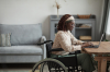 Une jeune femme en fauteuil roulant travaille à son bureau dans un appartement neuf adapté aux normes PMR