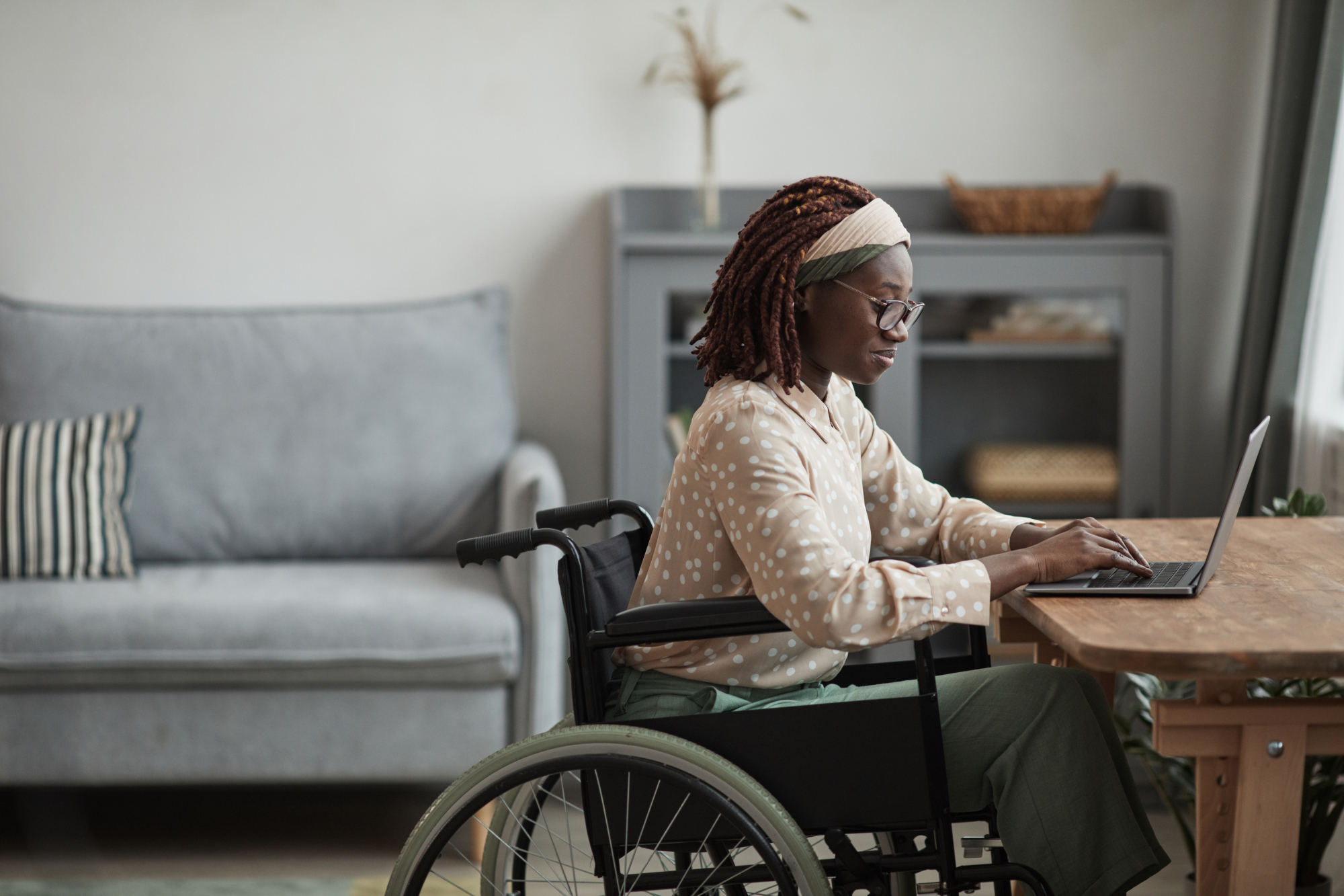 Une jeune femme en fauteuil roulant travaille à son bureau dans un appartement neuf adapté aux normes PMR