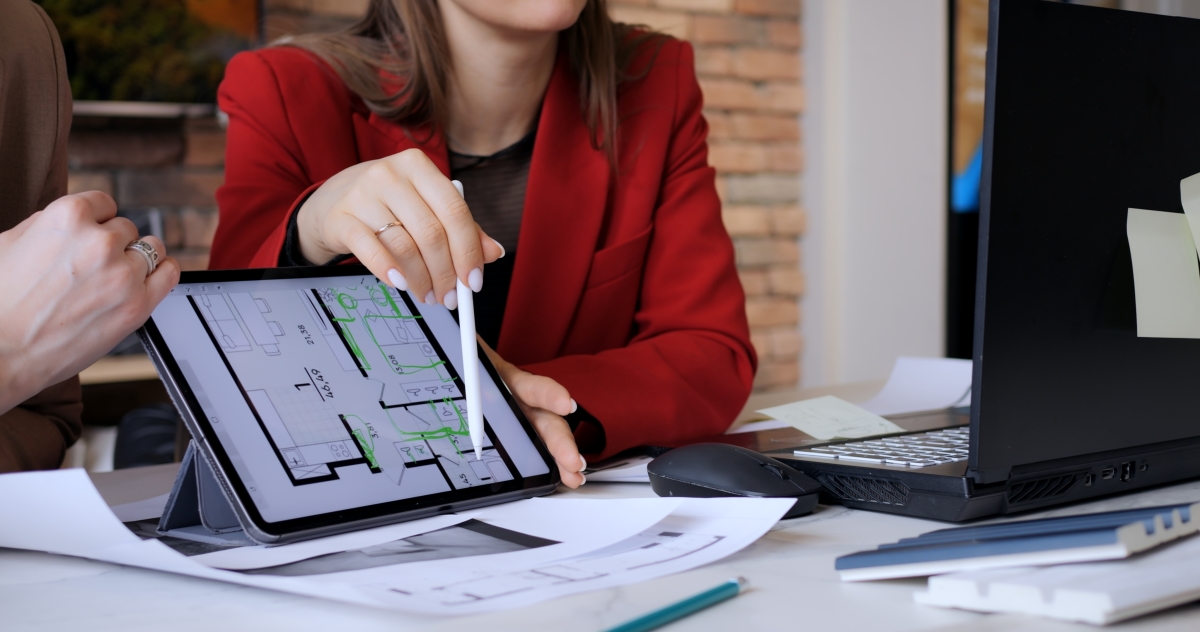 une main féminine montre un plan d’appartement sur une tablette numérique