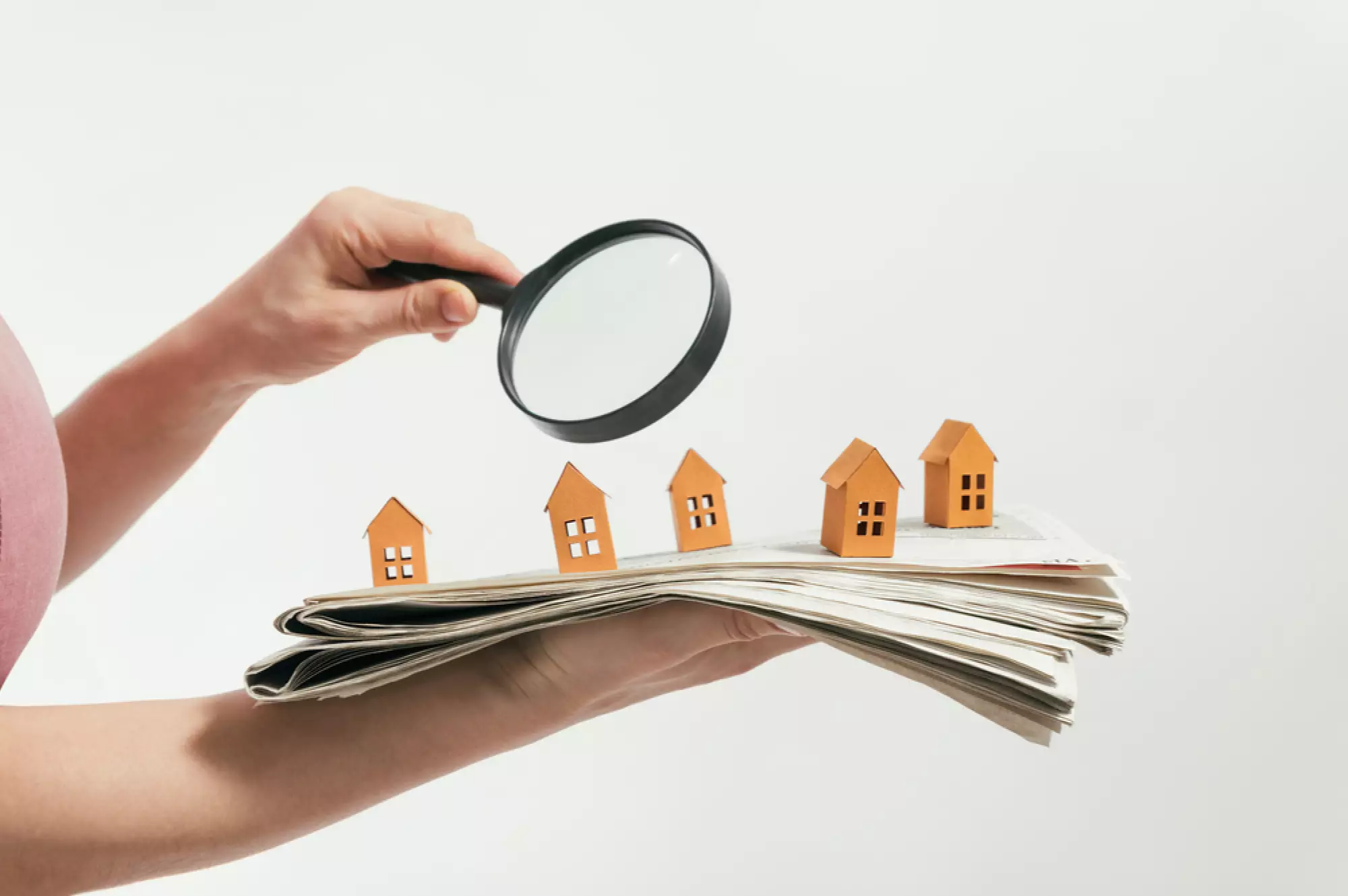 une femme regarde un journal surmonté de petites maisons en bois, à la loupe